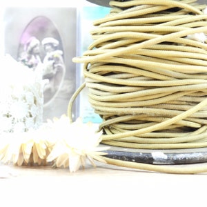 May include: A spool of beige cord wound around a wooden base. The cord is thick and has a slightly textured surface.