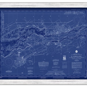 May include: A framed nautical chart of the St. Lawrence River, with detailed white lines and text on a blue background. The chart includes depth soundings and geographical features. The frame is white.