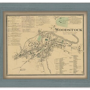 May include: An antique map of Woodstock, New York, printed in brown and black ink on cream paper. The map shows the layout of the town with streets, buildings, and landmarks. The title "Woodstock" is printed in large, bold letters at the top of the map. The map is framed in a light blue frame.