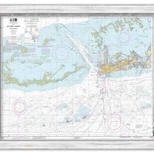 May include: A nautical chart of Key West Harbor and its approaches. The chart is printed in black and white with blue and green accents. The chart includes details such as depths, buoys, and navigational aids. The chart is framed in a white frame.