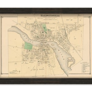 May include: An antique map of Baldwinsville, New York, printed in black and brown ink on cream paper. The map shows the town's streets, buildings, and waterways, including the Seneca River. The map is framed in a dark wood frame.