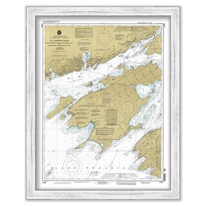May include: A vintage nautical chart of the St. Lawrence River, showing the area from Lake Ontario to the Thousand Islands. The chart is printed on a cream-colored paper with brown and blue lines. The chart is framed in a white frame.
