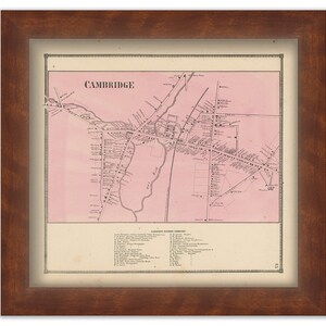 May include: An antique map of Cambridge, Massachusetts, printed on a pink background. The map shows the streets and buildings of the city, including Harvard University. The map is framed in a brown wooden frame.