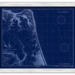 May include: A framed nautical map of Camp Pendleton and vicinity, rendered in a deep blue hue. The map features detailed coastlines, waterways, and grid lines, encased in a white wooden frame. The map is a vintage style nautical chart.