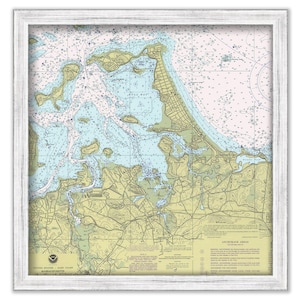May include: A nautical chart of the waters around Boston Harbor, Massachusetts. The chart is framed in a white wood frame and shows the coastline, islands, and waterways of the area. The chart is printed in blue, green, and brown colors. The text on the chart includes "UNITED STATES - EAST COAST - MASSACHUSETTS".