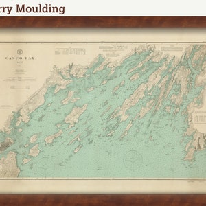 May include: A vintage map of Casco Bay, Maine, framed in a cherry wood frame. The map is printed on cream paper with blue and green accents. The title "Casco Bay, Maine" is printed in the top left corner.