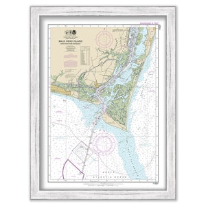 May include: A nautical chart of Bald Head Island, Cape Fear River Entrance, North Carolina. The chart is framed in a white wood frame. The chart shows the coastline, waterways, and depths of the area. The chart is printed in black, white, blue, green, and pink.