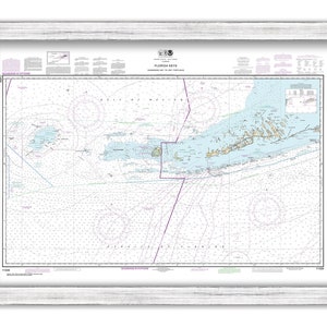 May include: A nautical chart of the Florida Keys, showing the islands and waterways from Key West to Key Largo. The chart is printed on paper and framed in a white wood frame.