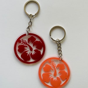 May include: Two keychains with silver key rings and chains. Each keychain features a red and orange hibiscus flower design.