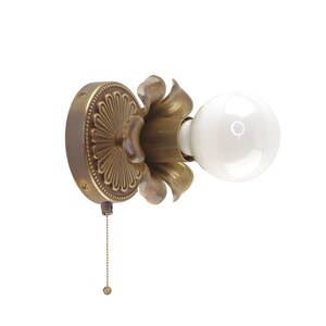 May include: A vintage-style wall sconce with a brass finish. The sconce features a decorative floral design around the light bulb and a pull chain. The light bulb is a round, white globe. The fixture is designed to be mounted on a wall.