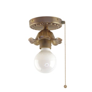 May include: A brass ceiling light fixture with a floral design and a pull chain. The light fixture has a white frosted glass bulb.
