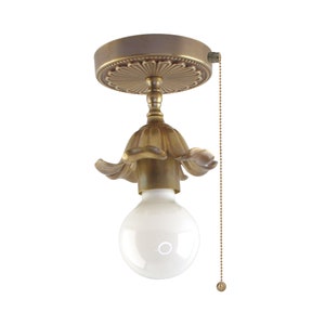 May include: A vintage-style ceiling light fixture with a brass finish. The fixture features a decorative floral design around the bulb and a pull chain. The light bulb is a round, white globe shape.