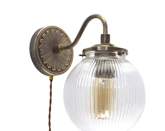 May include: A brass wall sconce with a clear ribbed glass globe shade. The sconce has a decorative floral design on the back plate.