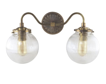 May include: A brass wall sconce with two clear glass globe shades. The shades have a ribbed texture and are illuminated by light bulbs.