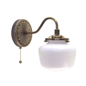 May include: A vintage-style wall sconce with a white glass shade and a brass finish. The sconce has a decorative floral design on the back plate and a pull chain switch.