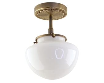May include: A brass ceiling light fixture with a white glass shade. The shade is a rounded dome shape. The fixture has a decorative brass plate with a floral design.