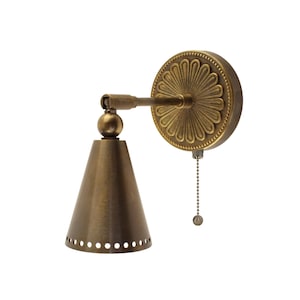 May include: Antique brass wall sconce with a cone-shaped shade and a decorative floral backplate. The sconce features a pull chain for easy operation and is designed for indoor lighting. The fixture has a vintage aesthetic.