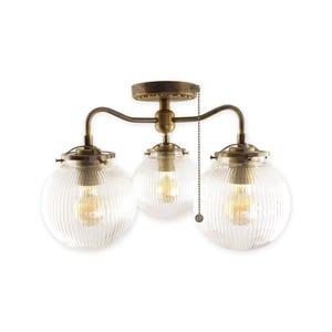 May include: A three-light ceiling fixture with a vintage design. It features three clear, ribbed glass globe shades, each housing a warm-toned light bulb. The fixture has a bronze-colored metal frame and a pull chain for operation.