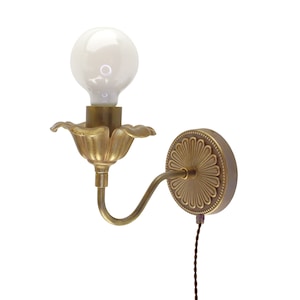 May include: A brass wall sconce with a flower-shaped shade and a round, decorative backplate. The sconce has a single light bulb and a long, brown cord.