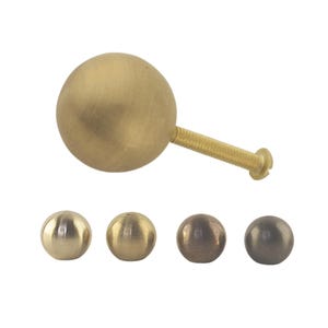 Könnte beinhalten: Ein Satz von vier runden Schrankknöpfen in verschiedenen Ausführungen: poliertes Messing, gebürstetes Messing, Antikmessing und Schwarznickel.