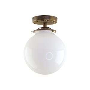 May include: A white glass globe ceiling light fixture with a brass finish. The fixture has a decorative brass plate with a floral design.