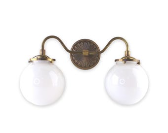 May include: A brass wall sconce with two white glass globe shades. The sconce has a decorative, ornate backplate.