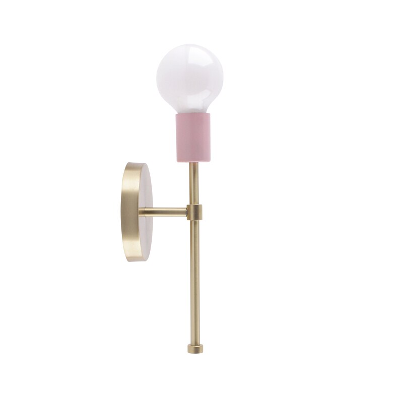 May include: A modern wall sconce with a gold-colored metal base and a pink bulb holder. The sconce features a white light bulb and a round, gold-colored wall mount. The design is minimalist and elegant, suitable for various interior styles.