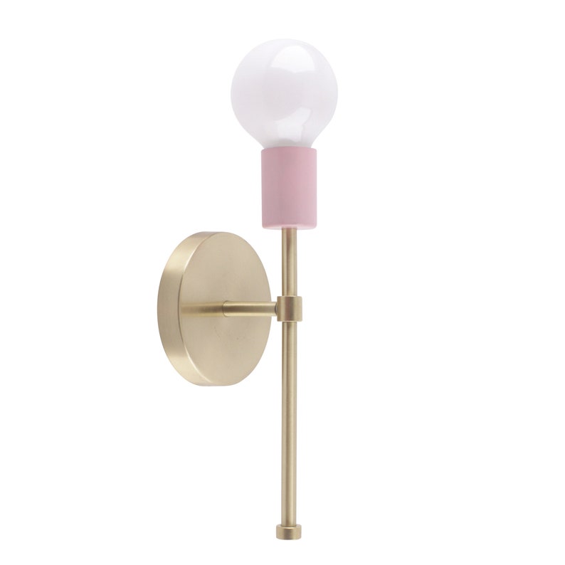 May include: A modern wall sconce with a gold-colored circular base and a slender, matching arm. The light fixture features a pink cylindrical accent and a white bulb. The design is minimalist and stylish.