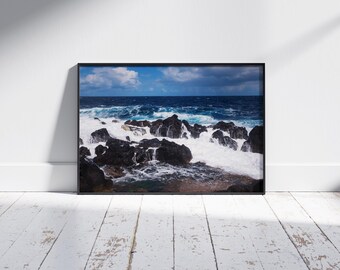 May include: A photograph of a rocky coastline with crashing waves. The water is a deep blue and the rocks are black. The waves are white and foamy.