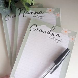 May include: Three green and white notepad sets with a floral design. The notepads have the words "Grandma", "Nanna", and "Great" written on them. Each notepad has the text "don't forget..." written on it. A black pen is lying on top of the "Grandma" notepad.
