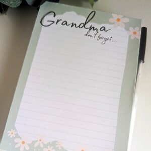 May include: A green notepad with a white lined interior and a white border with a floral design. The notepad has the text "Grandma don't forget..." at the top.