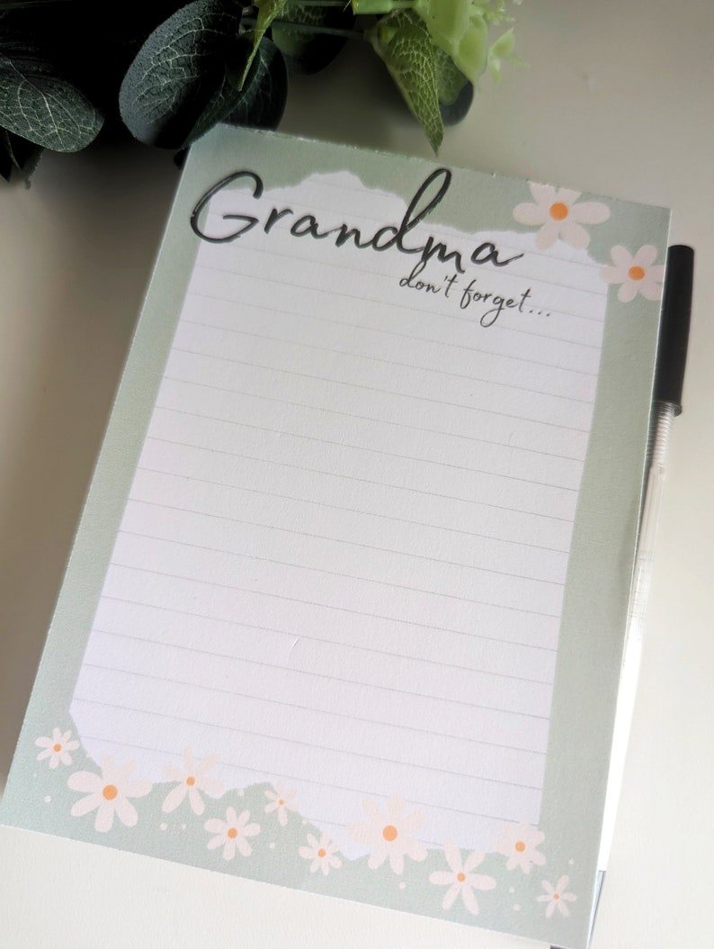May include: A green notepad with a white lined interior and a white border with a floral design. The notepad has the text "Grandma don't forget..." at the top.