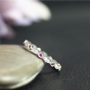 May include: A silver band ring with a row of small, oval-shaped diamonds and red gemstones.