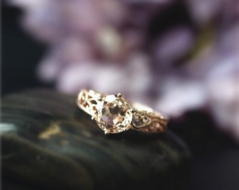 May include: A gold ring with a delicate filigree design and a large, round, light brown gemstone.