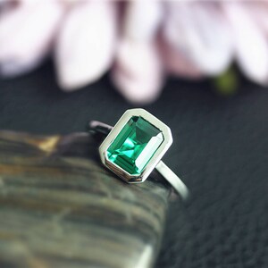 May include: A silver ring with a green emerald gemstone set in a square bezel.