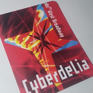Könnte beinhalten: Eine rote rechteckige Karte mit dem Wort "Cyberdelia" in weißen Blockbuchstaben. Die Karte zeigt ein Sternenmuster mit gelben und blauen Akzenten und dem Text "382 ½ West Broadway".