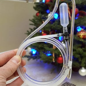 May include: A clear plastic tube with a clear plastic bulb on the end. The tube is bent into a loop and is held in a hand. The tube is likely used for a water bottle or other beverage container.