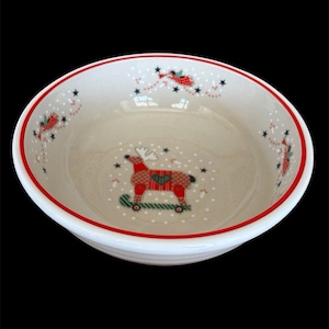 May include: A round ceramic bowl with a cream-colored interior featuring a red reindeer on a skateboard at the center. The rim is decorated with a thin red line and a pattern of small black stars, white dots, and red flying figures.