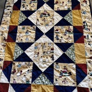 May include: A rectangular quilt featuring a central star pattern composed of navy blue, mustard yellow, and red dotted fabric triangles. The quilt blocks display a repeating print of children playing, interspersed with cream and floral fabric.