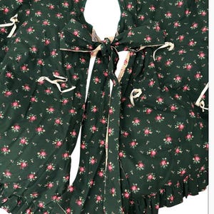 May include: A dark green fabric tree skirt featuring a repeating pattern of small pink roses and green leaves. The circular skirt has a central opening, a slit for placement, and is secured with cream-colored fabric ties and a ruffled edge.