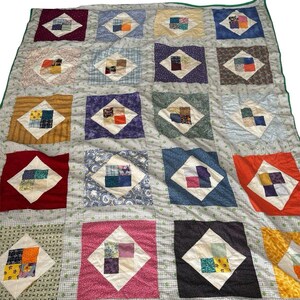 May include: A handmade quilt with a patchwork design. The quilt features a grid of squares, each with a diamond-shaped pattern in various colors like red, blue, and orange. The quilt is trimmed with a green border.