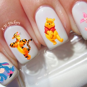 May include: Four white fingernails with Winnie the Pooh, Tigger, Piglet, and Eeyore nail art stickers. The stickers are colorful and feature the characters in various poses.
