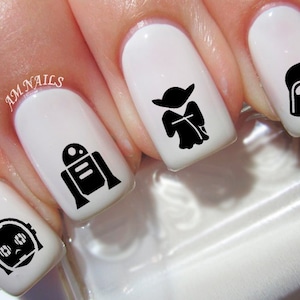 May include: White fingernails with black Star Wars character nail art decals. The characters include Yoda, Darth Vader, R2-D2, and C-3PO.