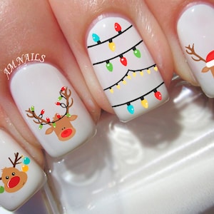 May include: White nail polish with Christmas themed nail art.  The nail art features reindeer with red noses and Christmas lights.