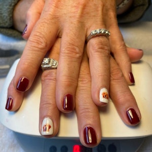 May include: Close-up of hands with burgundy nail polish and two nails with white dog face decals.