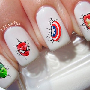 Puede incluir: Esmalte de u&ntilde;as blanco con pegatinas de arte de u&ntilde;as con tem&aacute;tica de superh&eacute;roes. Las pegatinas representan a Spiderman, Hulk, Iron Man y Capit&aacute;n Am&eacute;rica. Las pegatinas est&aacute;n dise&ntilde;adas para que parezca que los superh&eacute;roes est&aacute;n rompiendo una pared agrietada.