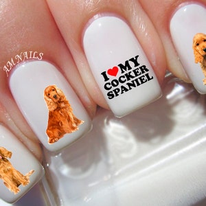 May include: White nail polish base featuring brown Cocker Spaniel dog graphics on three nails and black text that reads I LOVE MY COCKER SPANIEL with a red heart symbol. The text AM NAILS is printed in small white letters on one of the nails.