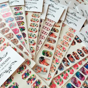May include: Assortment of nail stickers with various designs, including floral patterns, pin-up girls, and abstract art. The stickers are packaged in clear plastic bags with white labels that read "MAM STICKERS - NAIL DECALS".
