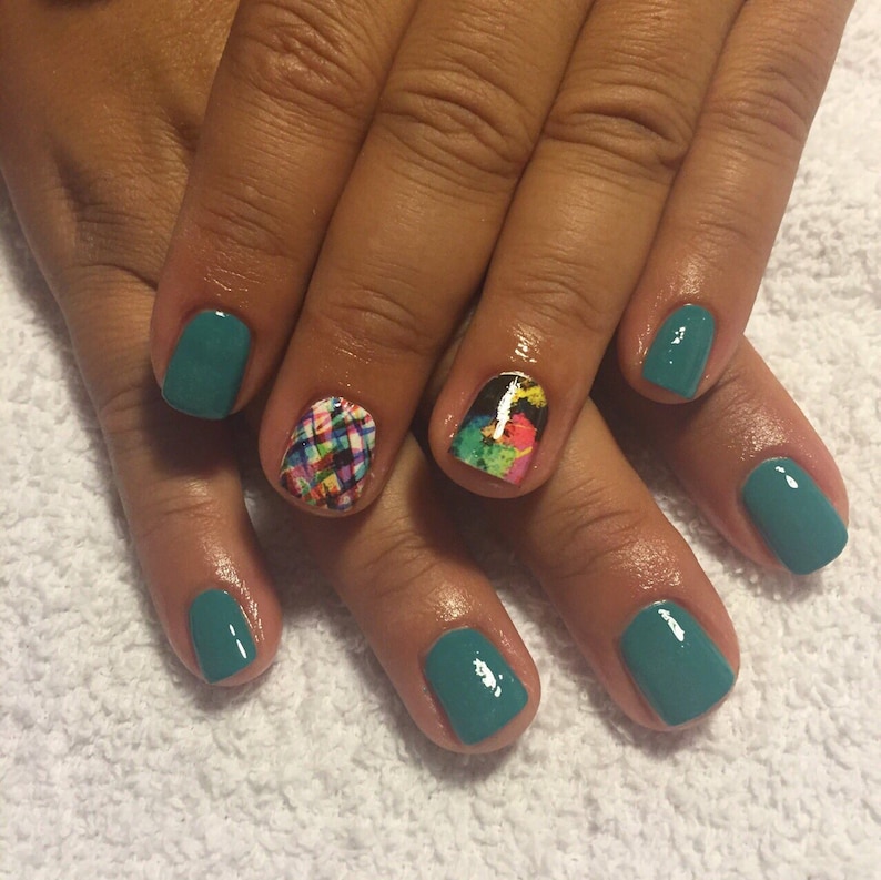 May include: Close-up of a hand with teal nail polish and two accent nails. One accent nail has a colorful abstract design, and the other has a colorful plaid design.