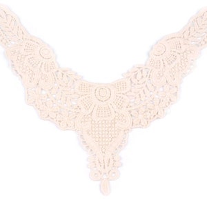 Op de afbeelding: Een delicate, crèmekleurige kanten kraag met een gegolfde rand en ingewikkelde bloemmotieven. De kraag is perfect om een ​​toets van elegantie toe te voegen aan elk kledingstuk.